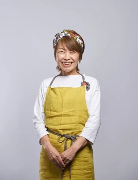 黄色いエプロン姿で微笑む発起人の岡村菜穂子